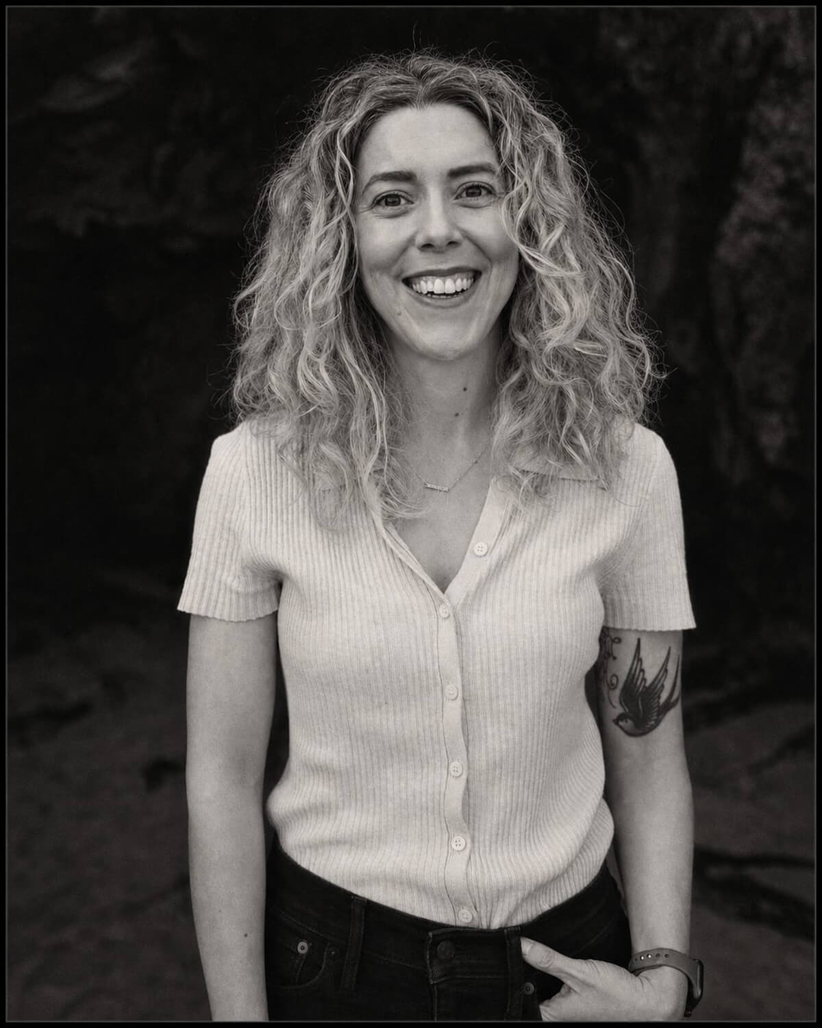 Black and white portrait of Nikole Sparks, smiling, with long curly hair, wearing a light short-sleeve top
